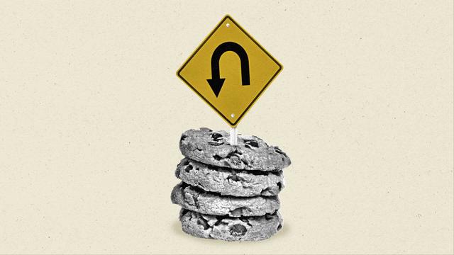 A U-Turn street sign sticks out of a stack of chocolate chip cookies.
