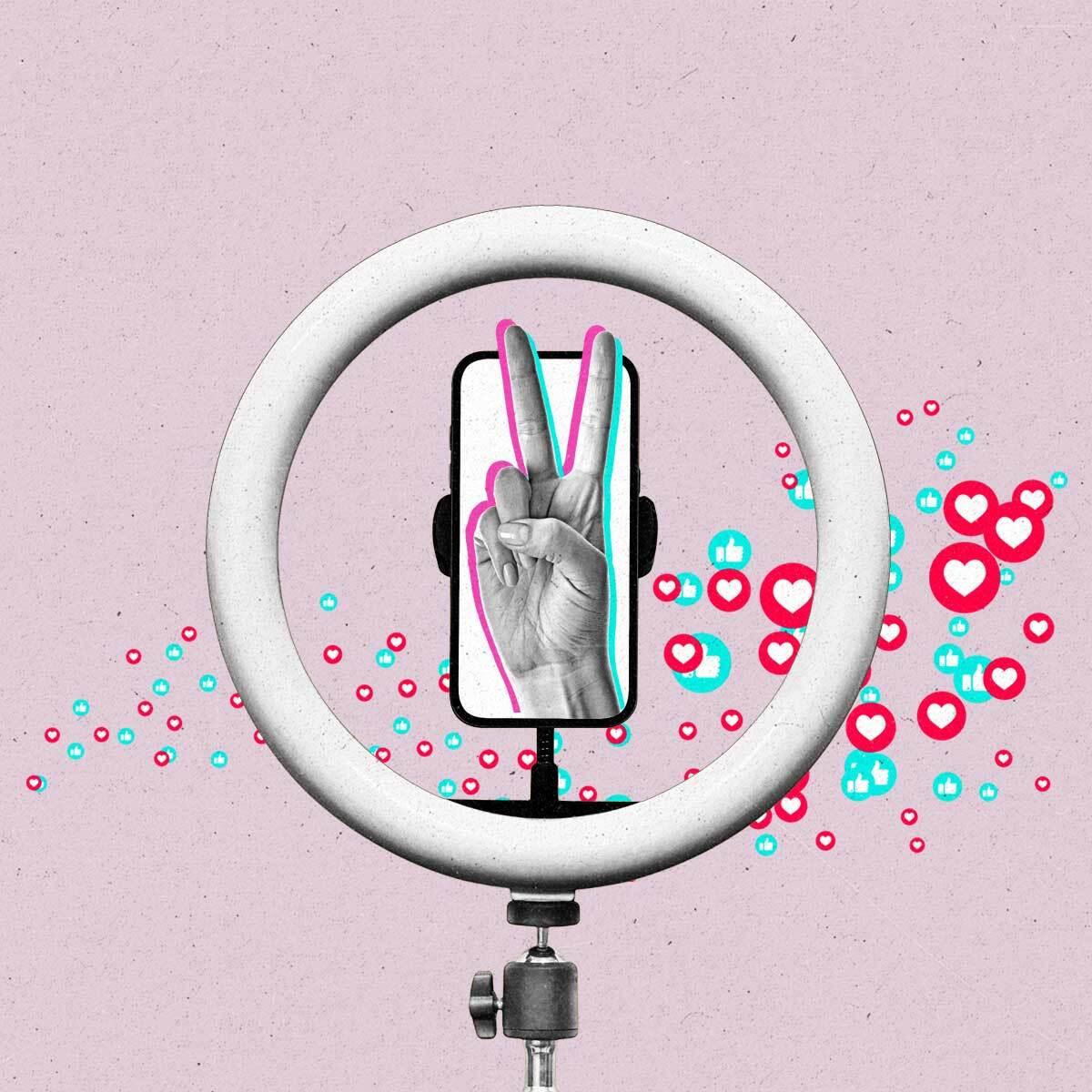 A hand making a peace sign sticks out of a smartphone within a ring light as like and love emoji float across it.